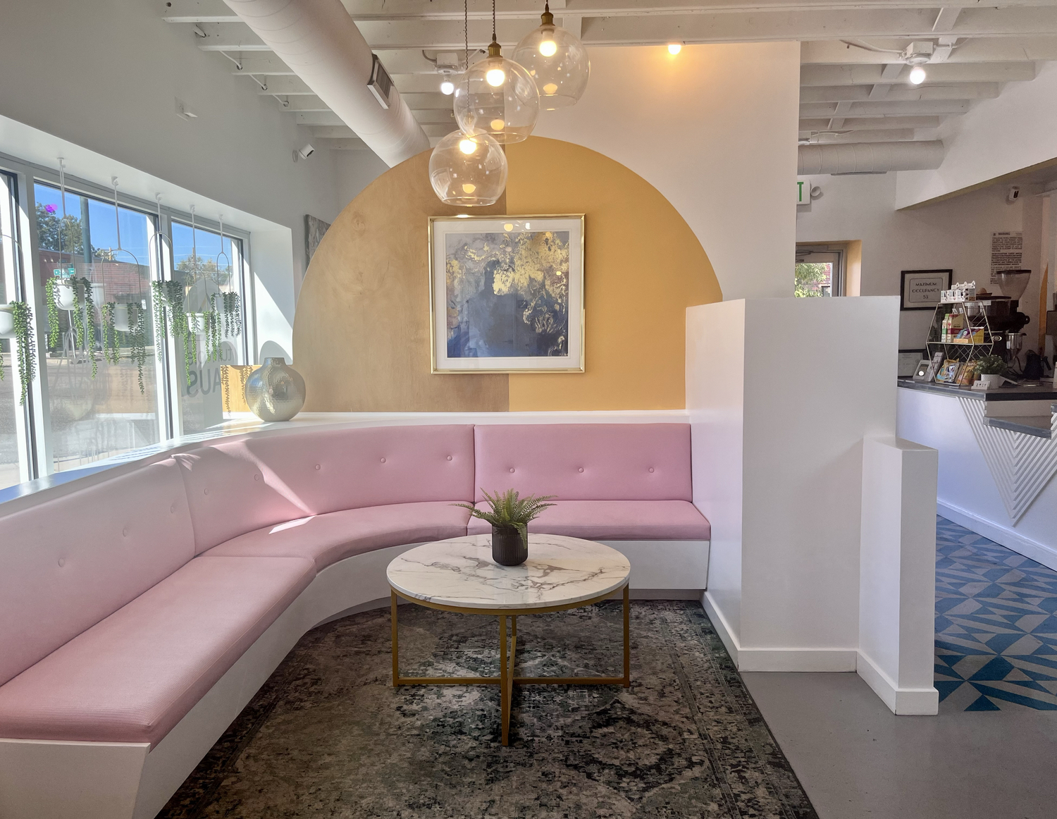 Bright cafe seating area at tumble HAUS Denver with pink booth seating, marble table and pendant lighting